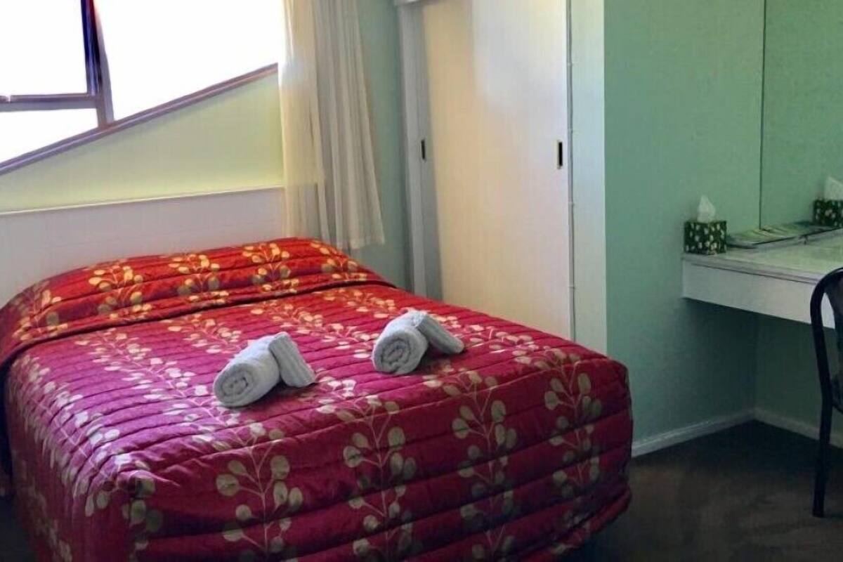 A bedroom with a bed, a desk, and a window.