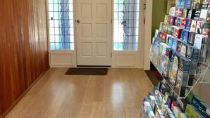 A room with wooden walls, a wooden floor, a white door with glass panels, and a magazine rack on the right.
