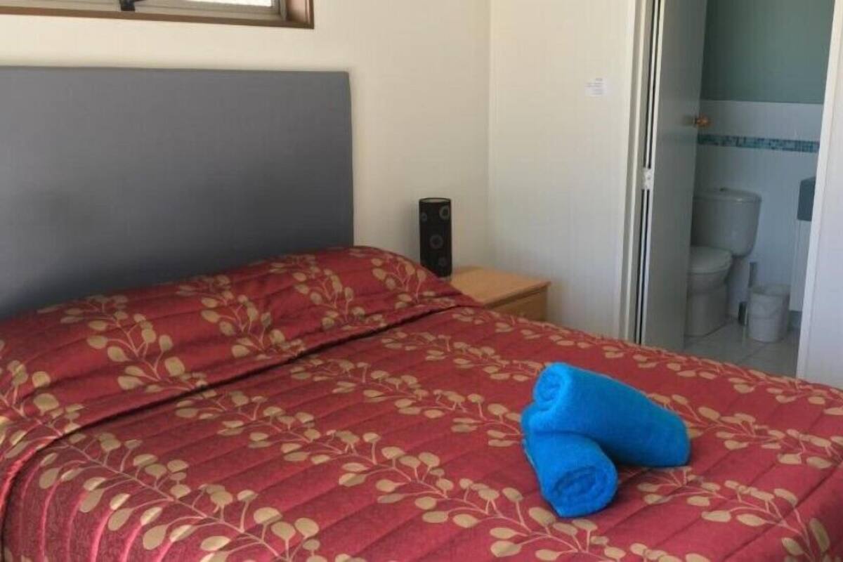 A single bed with a floral-patterned bedspread, a wooden nightstand, and a bathroom visible through an open door.