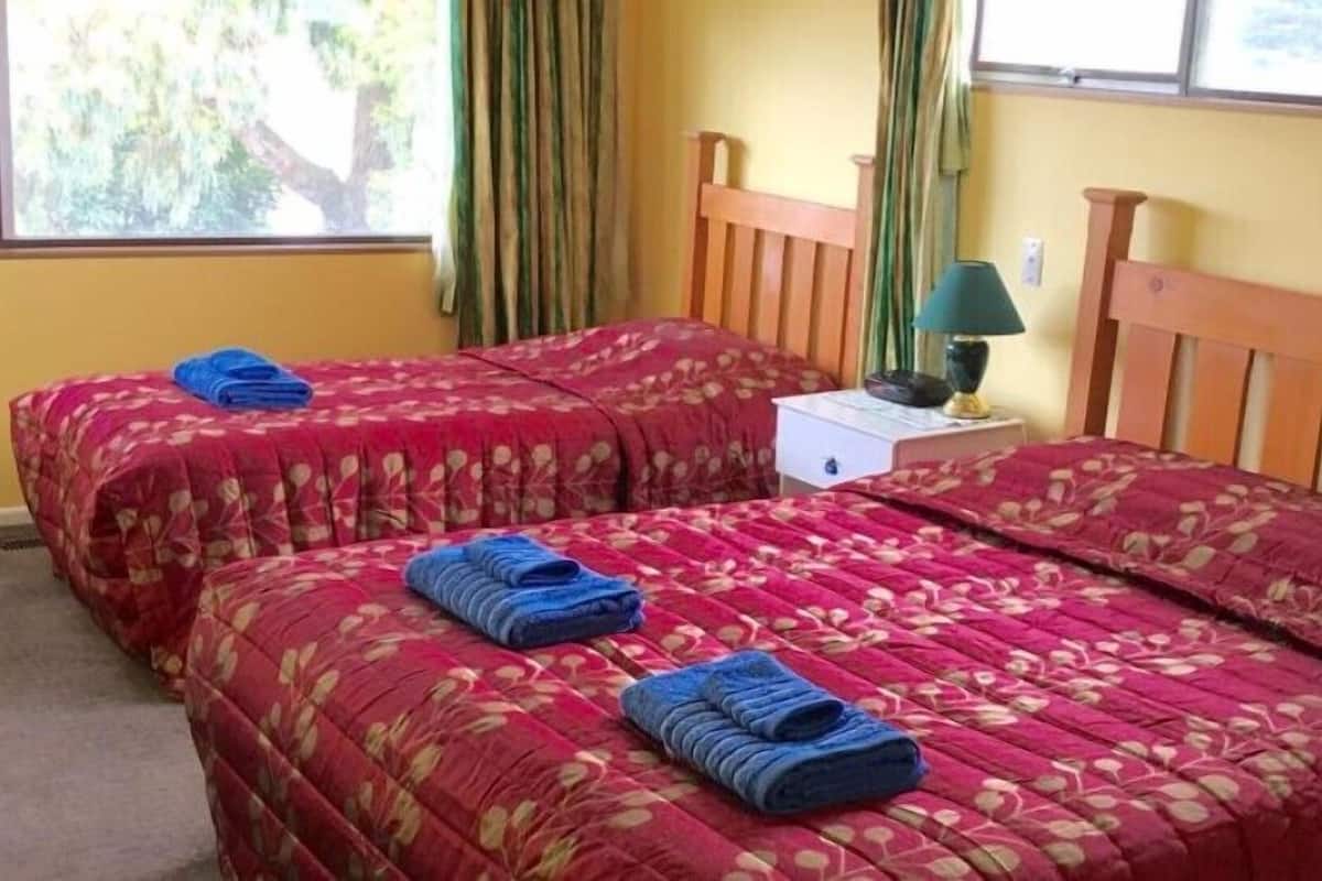 A room with two beds, each with a floral-patterned bedspread and blue towels. There is a nightstand with a lamp and a small drawer.