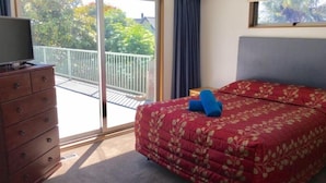 A bedroom with a bed, a dresser, and a balcony.