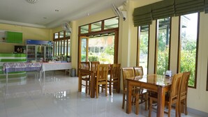 A spacious dining area with a large wooden table and chairs, a refrigerator with beverages, and a green counter with a menu. - Aranya Resort (Chumphon)