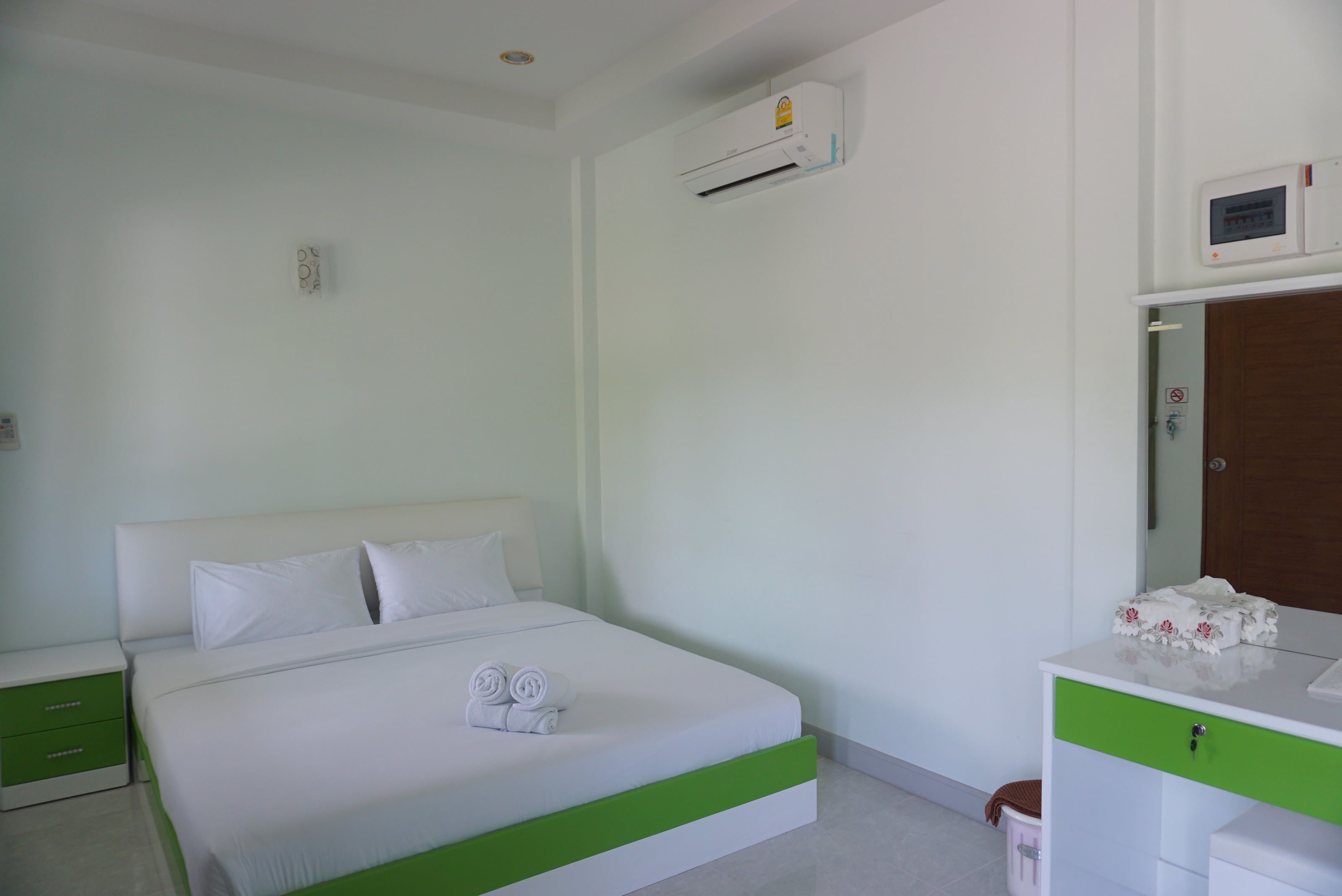 Habitació d'hotel amb un llit individual, una taula de nit verda, un calaix blanc i un aire condicionat fixat a la paret.