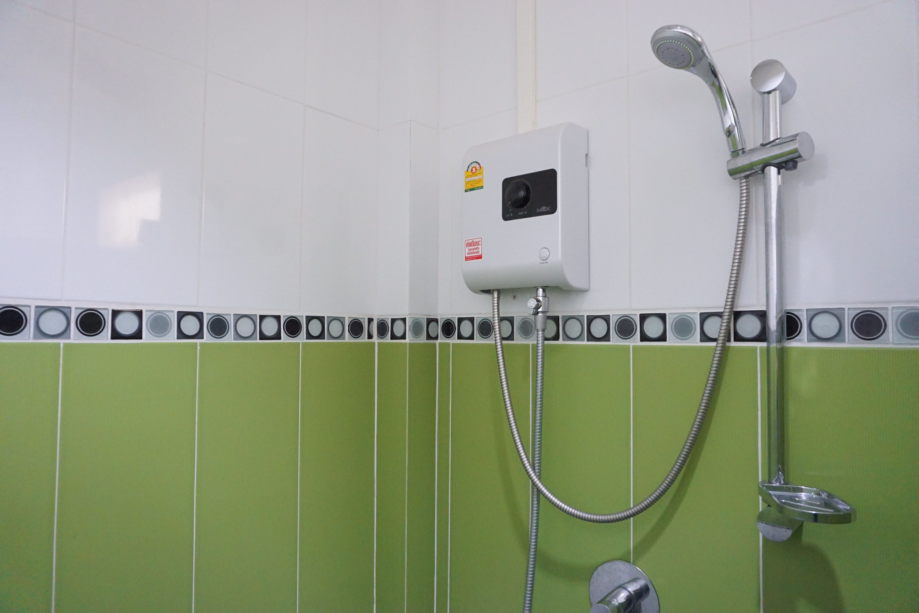 A bathroom with a white and green tiled wall, a built-in heater, and a shower with a handheld showerhead and a fixed showerhead.