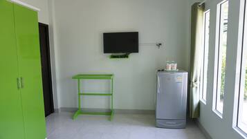 A room with a green wardrobe, a wall-mounted TV, a Hitachi refrigerator, and a window with curtains.