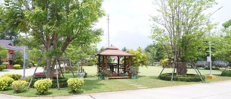 A gazebo in a park with surrounding trees and a clear sky.