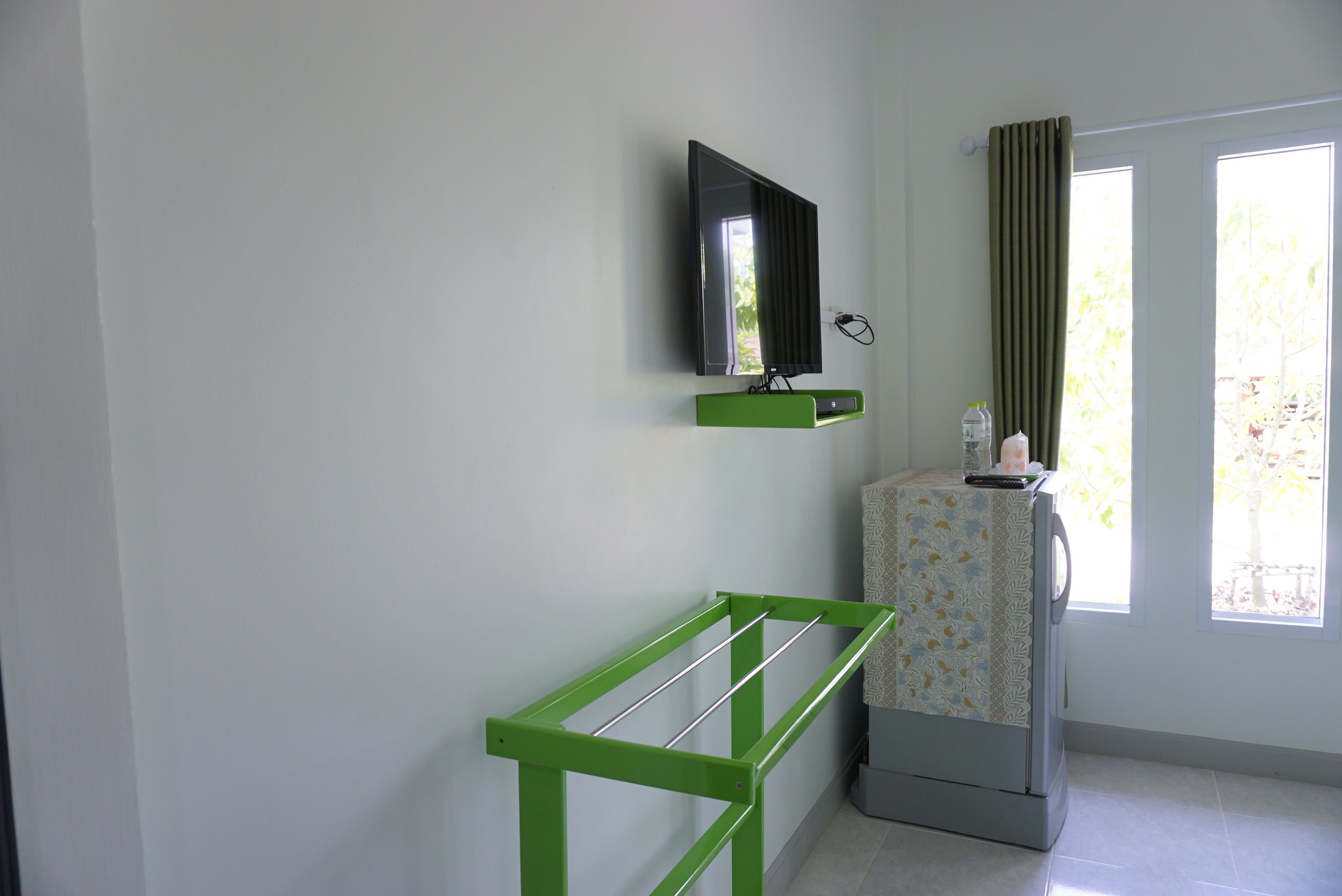 Una habitación con una estantería metálica verde, un televisor de pantalla plana montado en la pared y un refrigerador con un forro estampado.