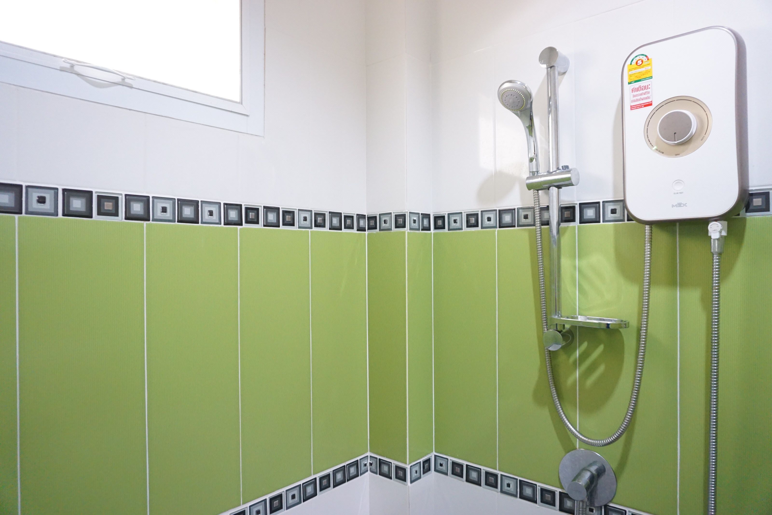A bathroom with green tiles, a shower, and a wall-mounted water heater.