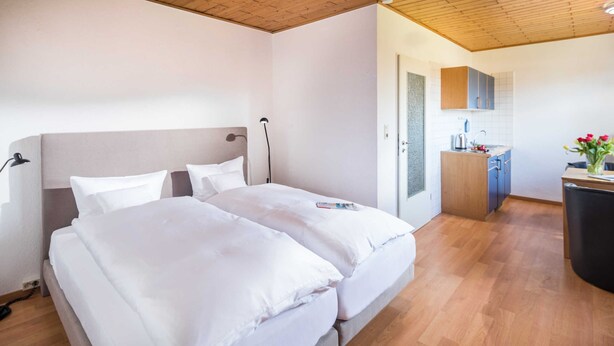 A double bed with white linens, a wooden ceiling, and a small kitchenette with a sink and cabinets.