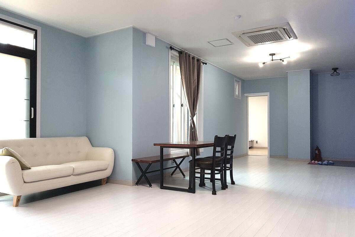 A room with a white sofa, a dining table with chairs, and a window with curtains.