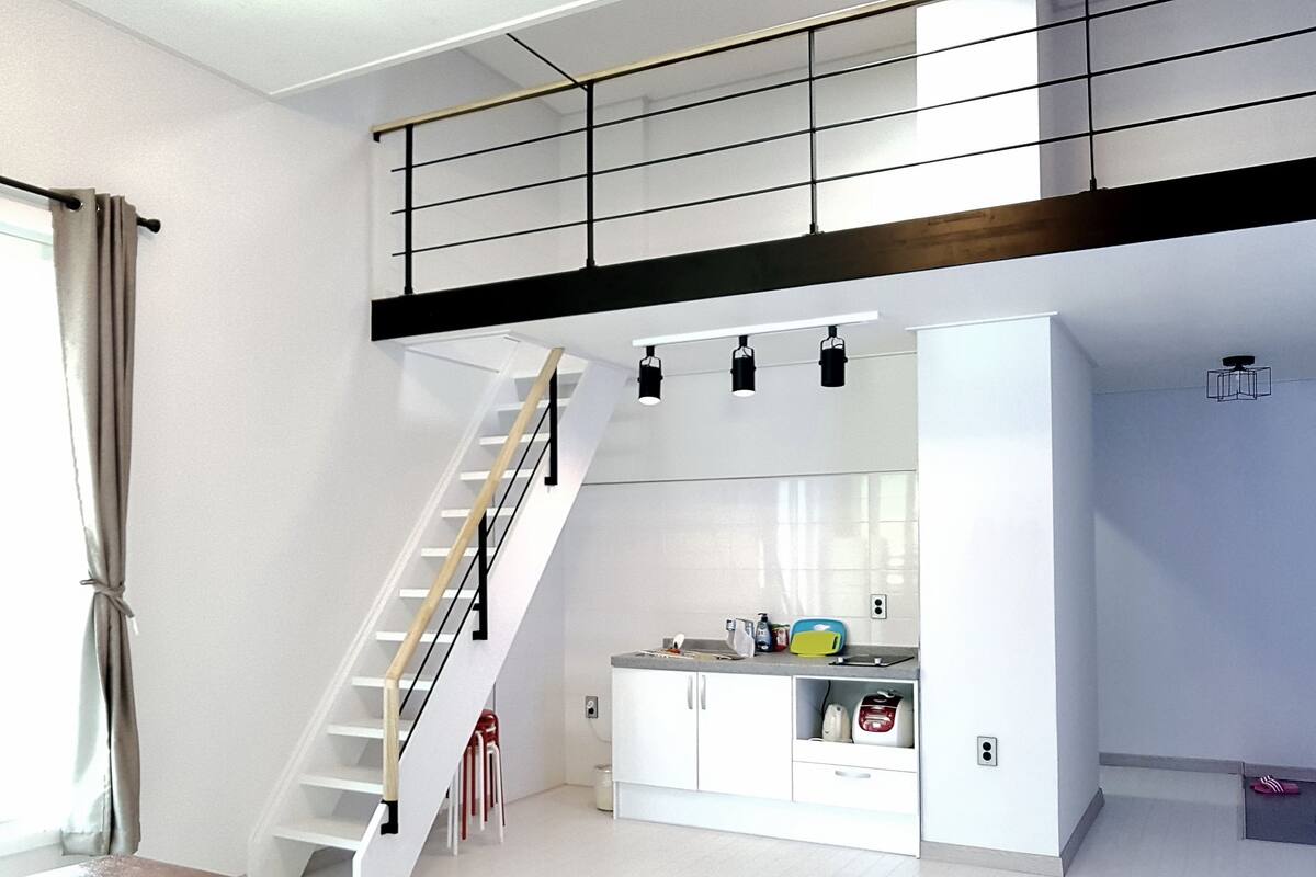 A modern kitchen with white cabinets, a wooden staircase, and a mezzanine level with black railings.