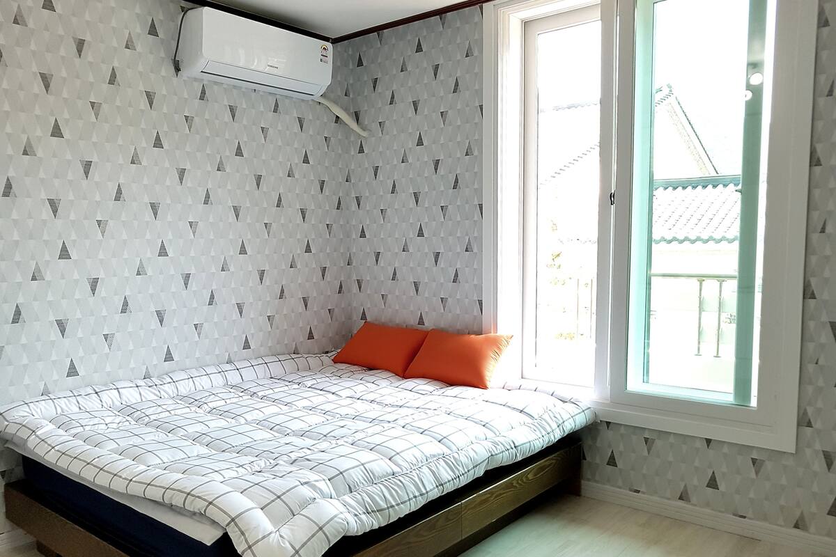A bedroom with a bed, a window, and a wall-mounted air conditioner.