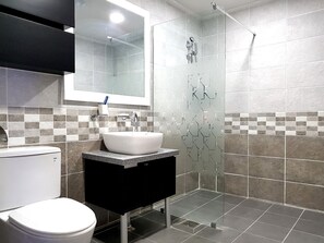 A modern bathroom with a white sink, black vanity, and a glass shower enclosure. - You & I Pension (Gumi)