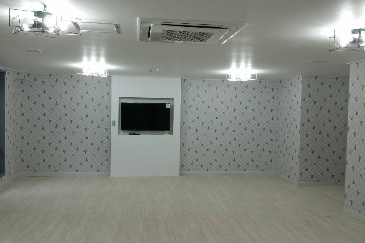 A room with patterned wallpaper, a mounted TV, recessed lighting, and an air conditioning unit.