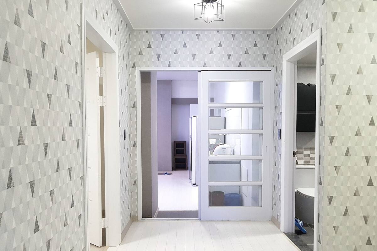 A hallway with patterned wallpaper, a white door leading to a room with a white ceiling, and a ceiling light fixture.