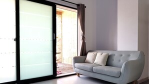 Una sala de estar moderna con un ventanal corredera que da a un balcón, un sofá gris y piso de madera.