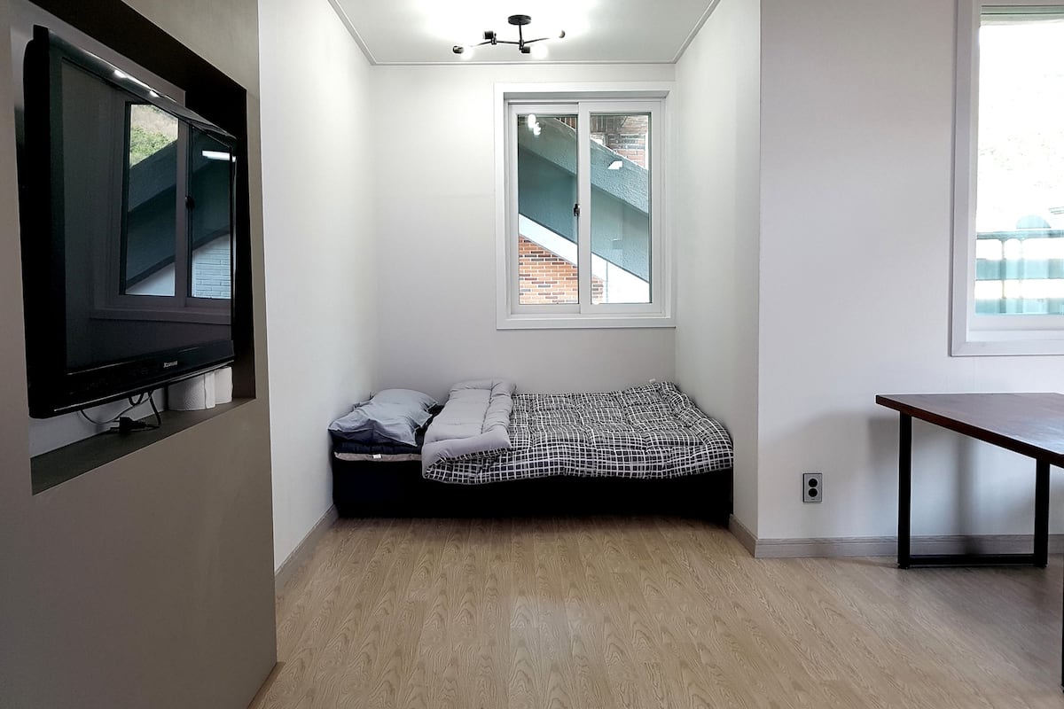 A small, bright room with a bed, a TV, and a window with a view of a staircase.