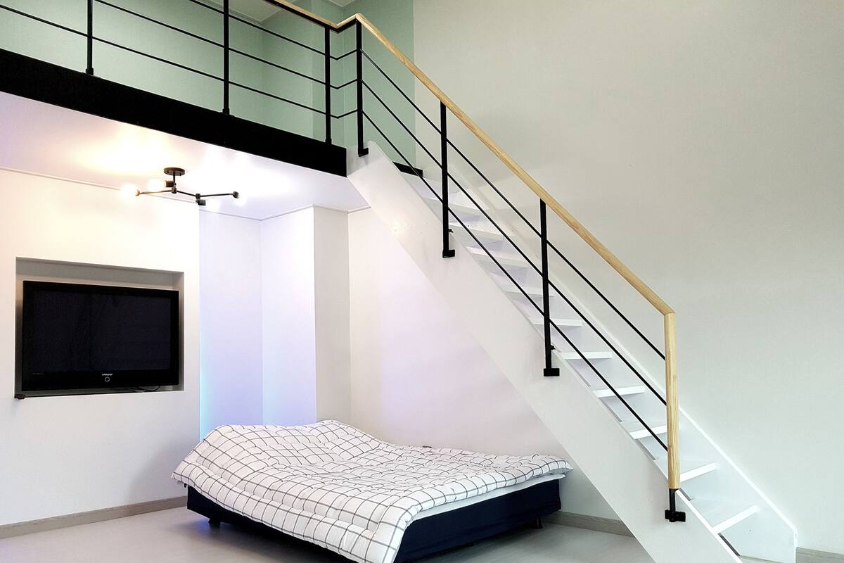 A bedroom with a bed, a TV mounted on the wall, and a staircase with a wooden handrail.
