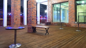 Un área de patio al aire libre con pilares de ladrillo, suelo de madera y mesas.