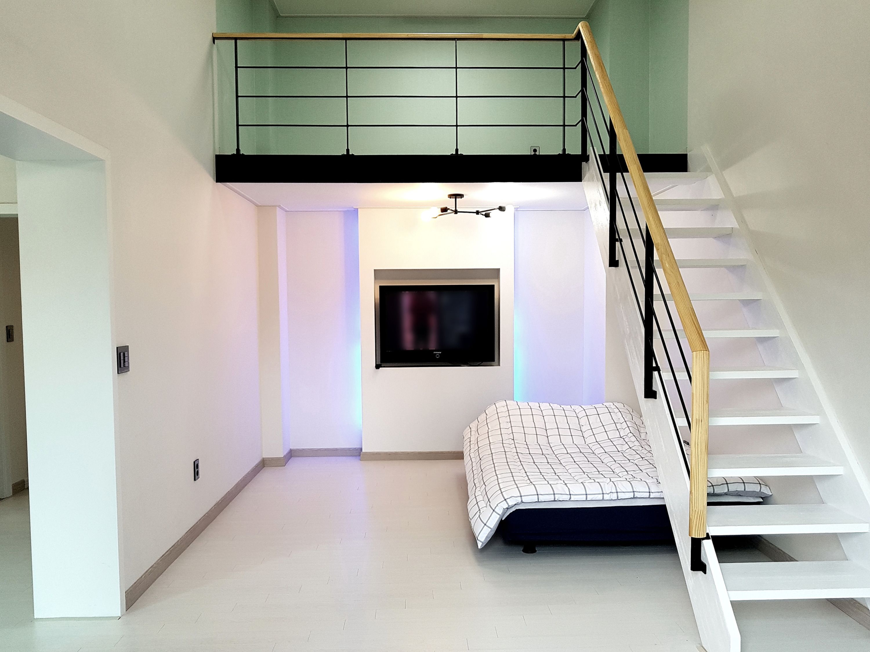 A modern loft bedroom with a loft bed, a television, and a staircase.