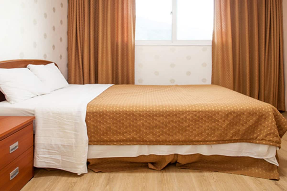 A neatly made bed with a wooden headboard, a wooden nightstand with drawers, and a window with curtains.