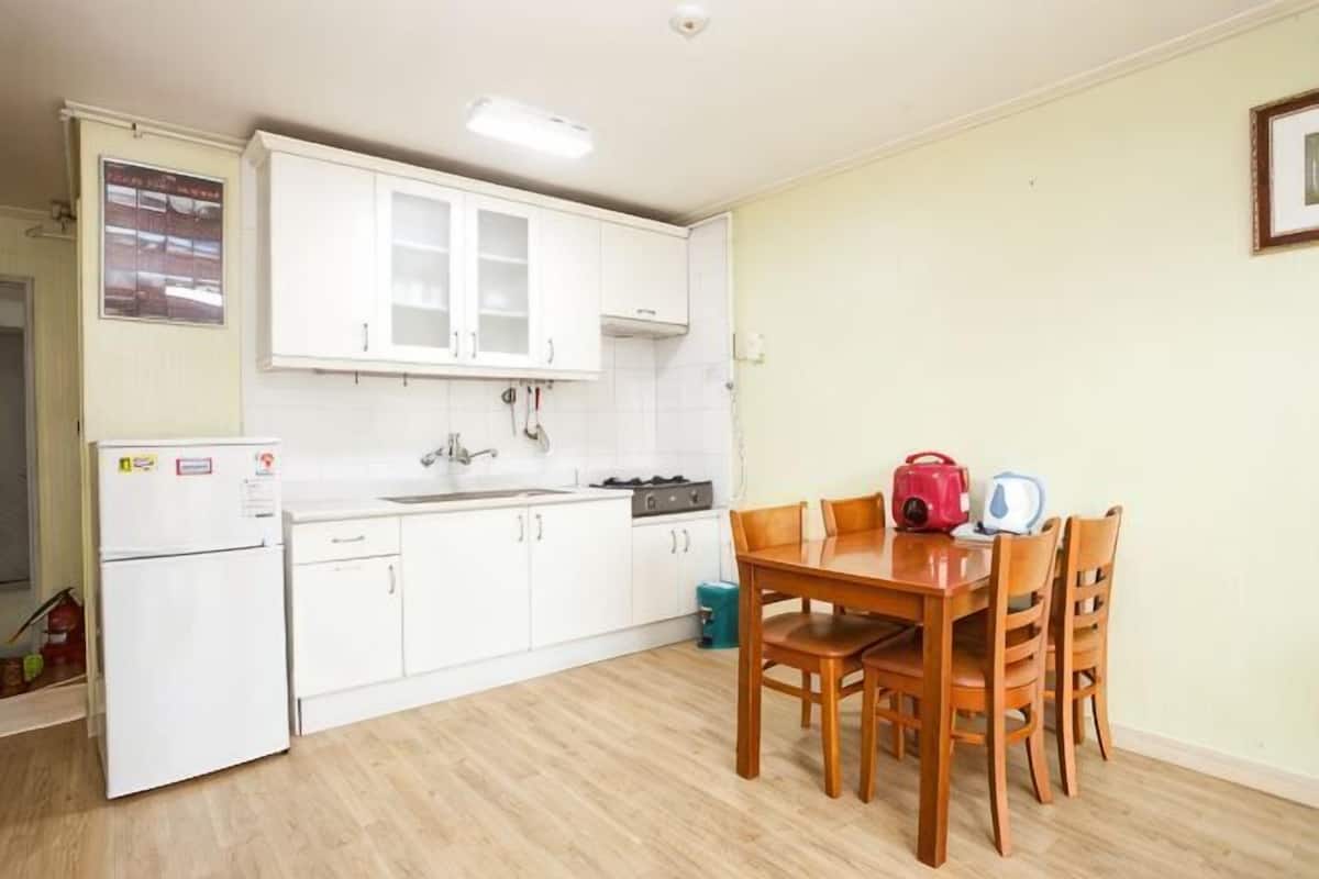 A compact kitchen with white cabinets, a refrigerator, a sink, and a dining table with chairs.