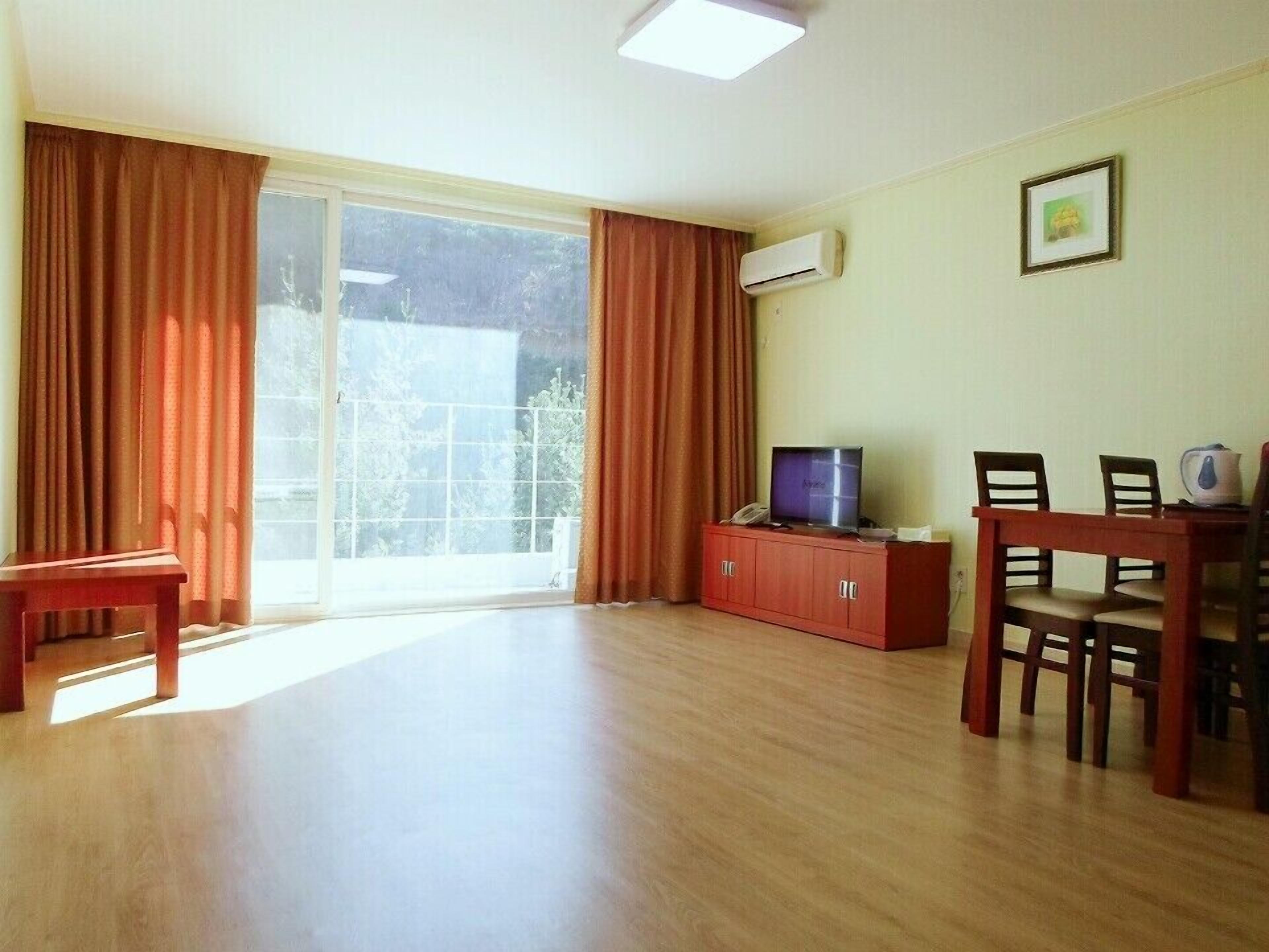 A room with a large sliding glass door, a television on a wooden cabinet, a dining table with chairs, and a framed picture on the wall.