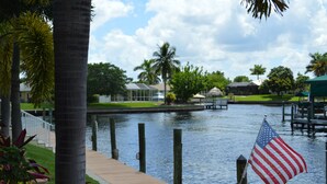 A waterfront view with a dock, palm trees, and an American flag. - Villa near Cape Harbor, with large pool, whirlpool (Cape Coral)