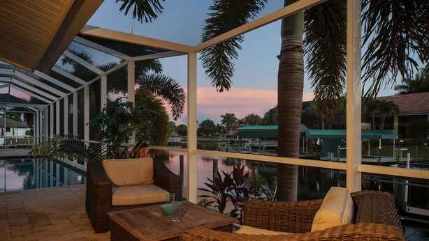 A sunlit outdoor seating area with wicker furniture and a view of a marina. - Villa near Cape Harbor, with large pool, whirlpool (Cape Coral)