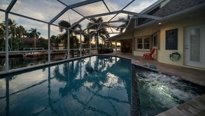 A swimming pool with a glass enclosure, surrounded by palm trees and a dock with boats. - Villa near Cape Harbor, with large pool, whirlpool (Cape Coral)