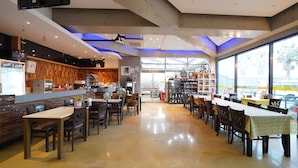 A restaurant with a bar area, dining tables, chairs, and a large window providing a view outside. - Jeju IN Hotel (Jeju City)