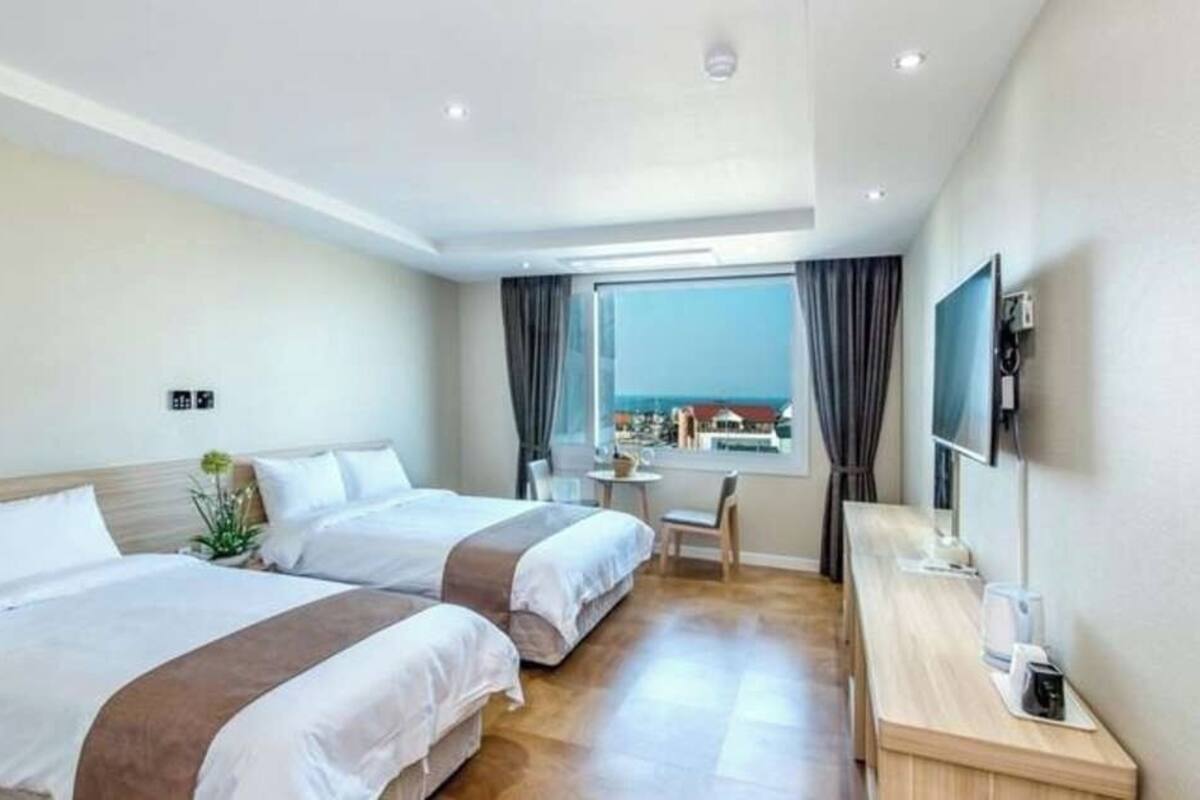 Ein Hotelzimmer mit zwei Betten, einem Schreibtisch, einem Fernseher und einem Fenster mit Blick.