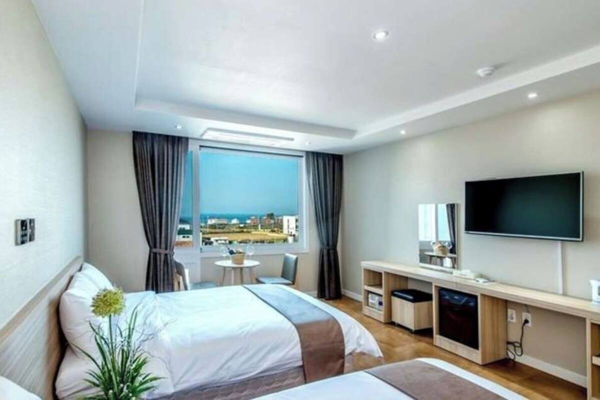 Ein Hotelzimmer mit zwei Betten, einem Fernseher, einem Schreibtisch mit Stuhl, einem kleinen Tisch und Blick auf die Stadt.