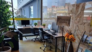 A modern business center with a marble wall, a sign indicating the business center, a desk with a computer, chairs, and potted plants. - Jeju IN Hotel (Jeju City)