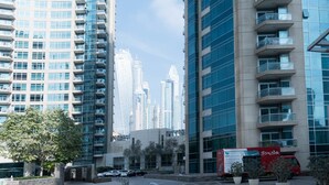 A modern urban street with high-rise buildings, a paved road, and a delivery truck. - Park Island - Bonaire by Deluxe Holiday Homes (Dubai)