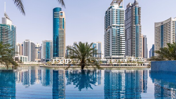 A modern urban skyline with high-rise buildings and a clear blue pool reflecting the surroundings. - Park Island - Bonaire by Deluxe Holiday Homes (Dubai)