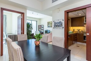 A dining area with a dark table, striped chairs, a potted plant, and a view into a living room and kitchen. - Standpoint A by Deluxe Holiday Homes (Dubai)