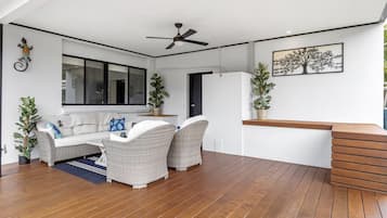 Una sala de estar moderna con un sofá, dos sillones de mimbre, una mesa de centro de madera y un ventilador de techo.