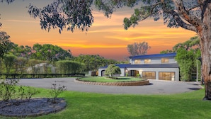 A modern house with a large driveway, surrounded by well-maintained lawns and trees. - Elk Estate (Inverloch)