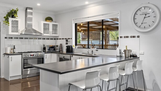 A modern kitchen with a large island, white cabinetry, stainless steel appliances, and a clock on the wall. - Elk Estate (Inverloch)