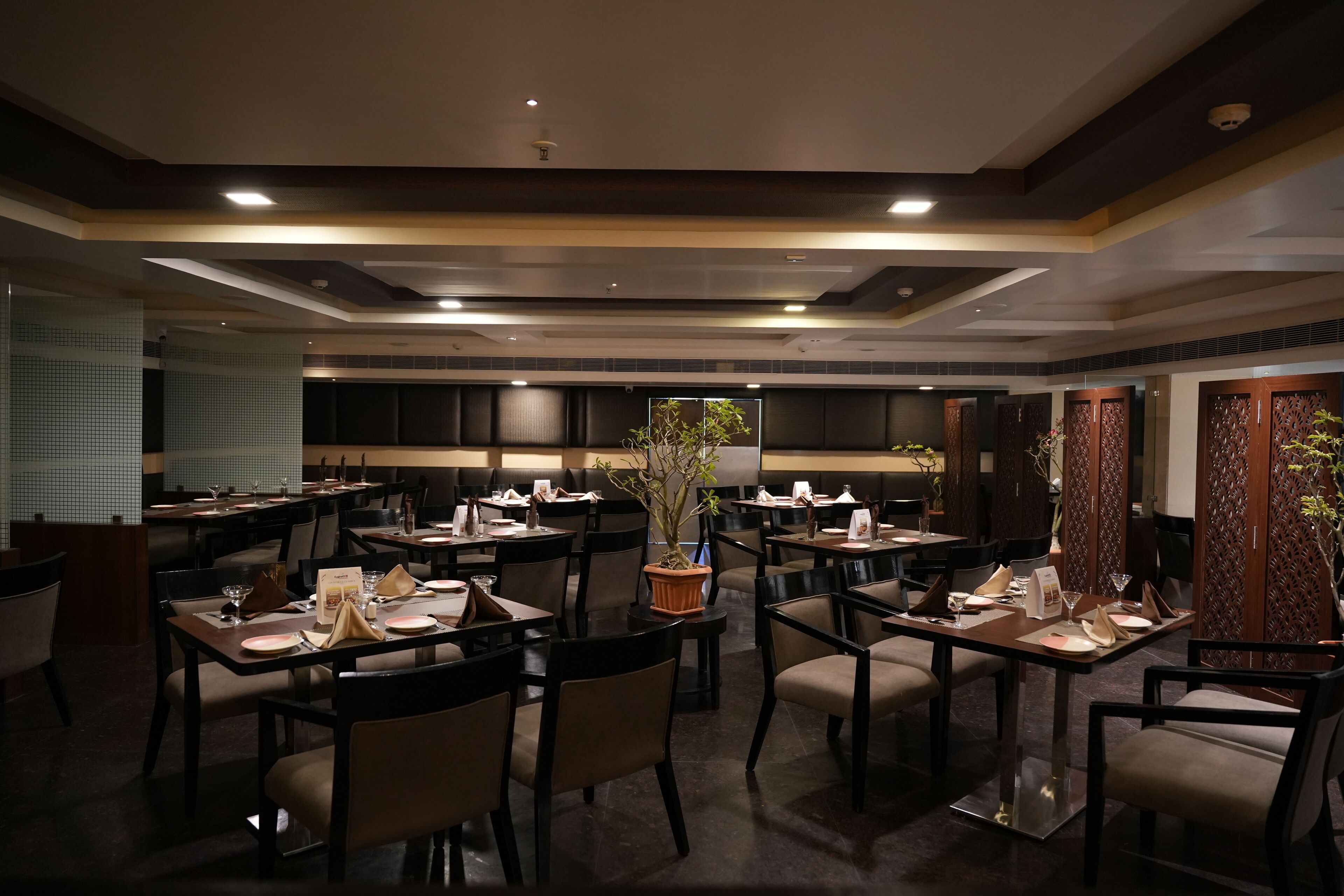 A restaurant with multiple tables and chairs, each set with plates, glasses, and napkins.