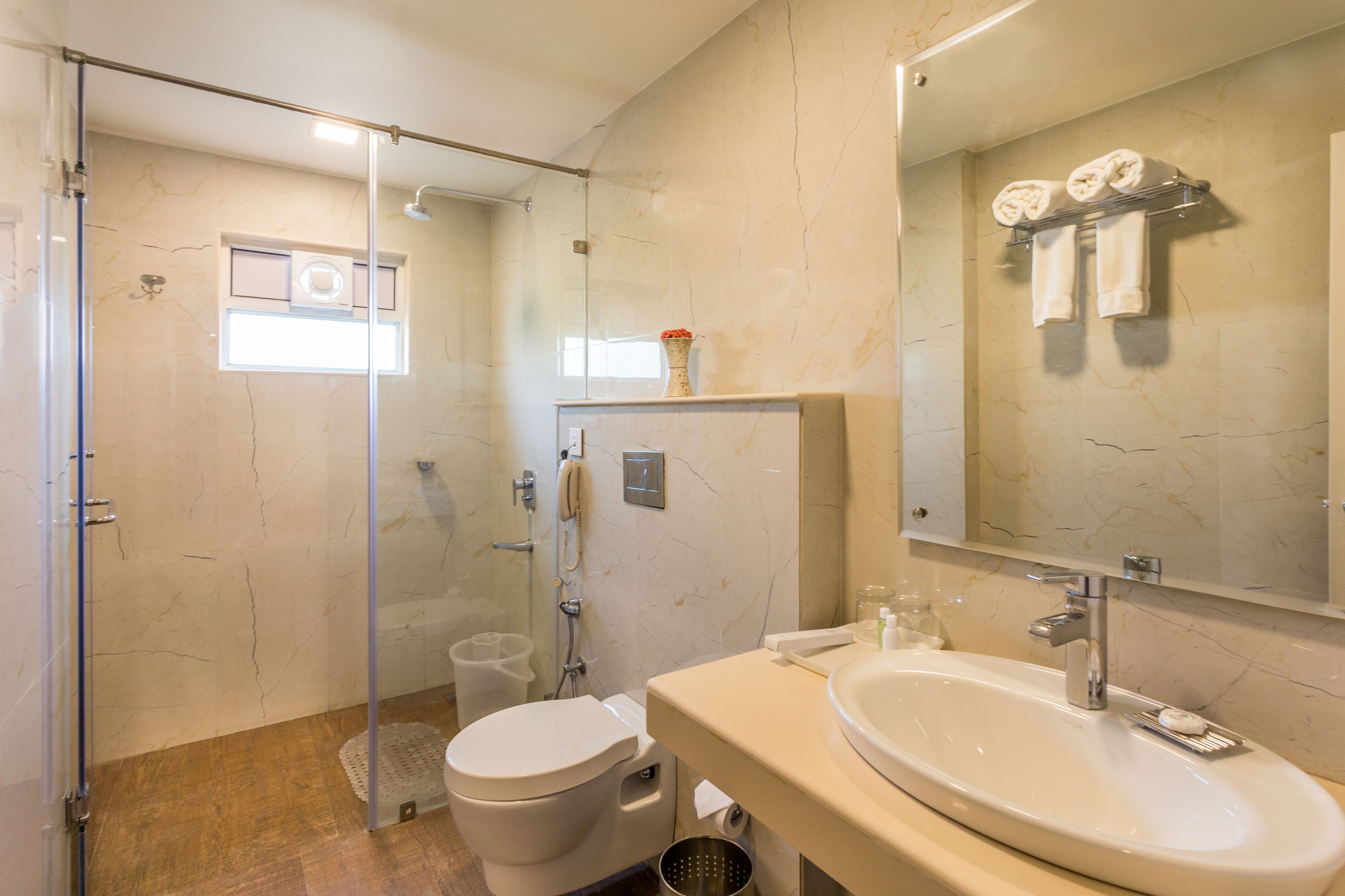 Un baño moderno con ducha de vidrio, inodoro blanco, lavamanos con espejo y toallero con toallas.
