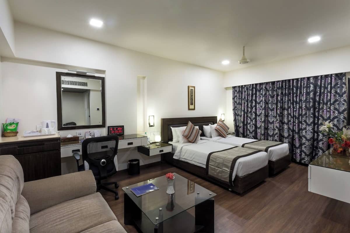 A hotel room with two beds, a desk, a chair, a coffee maker, a clock, and a mirror.