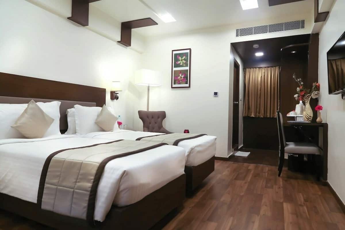 A hotel room with a large bed, a desk, and a chair. There is a lamp and a picture on the wall.