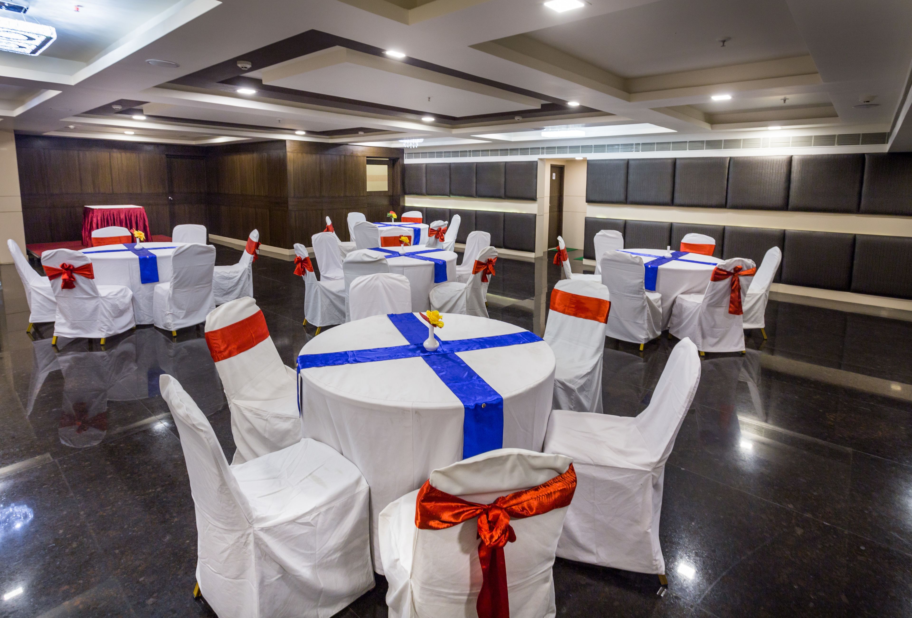 A conference room with round tables, white chairs with red sashes, and dark padded walls.