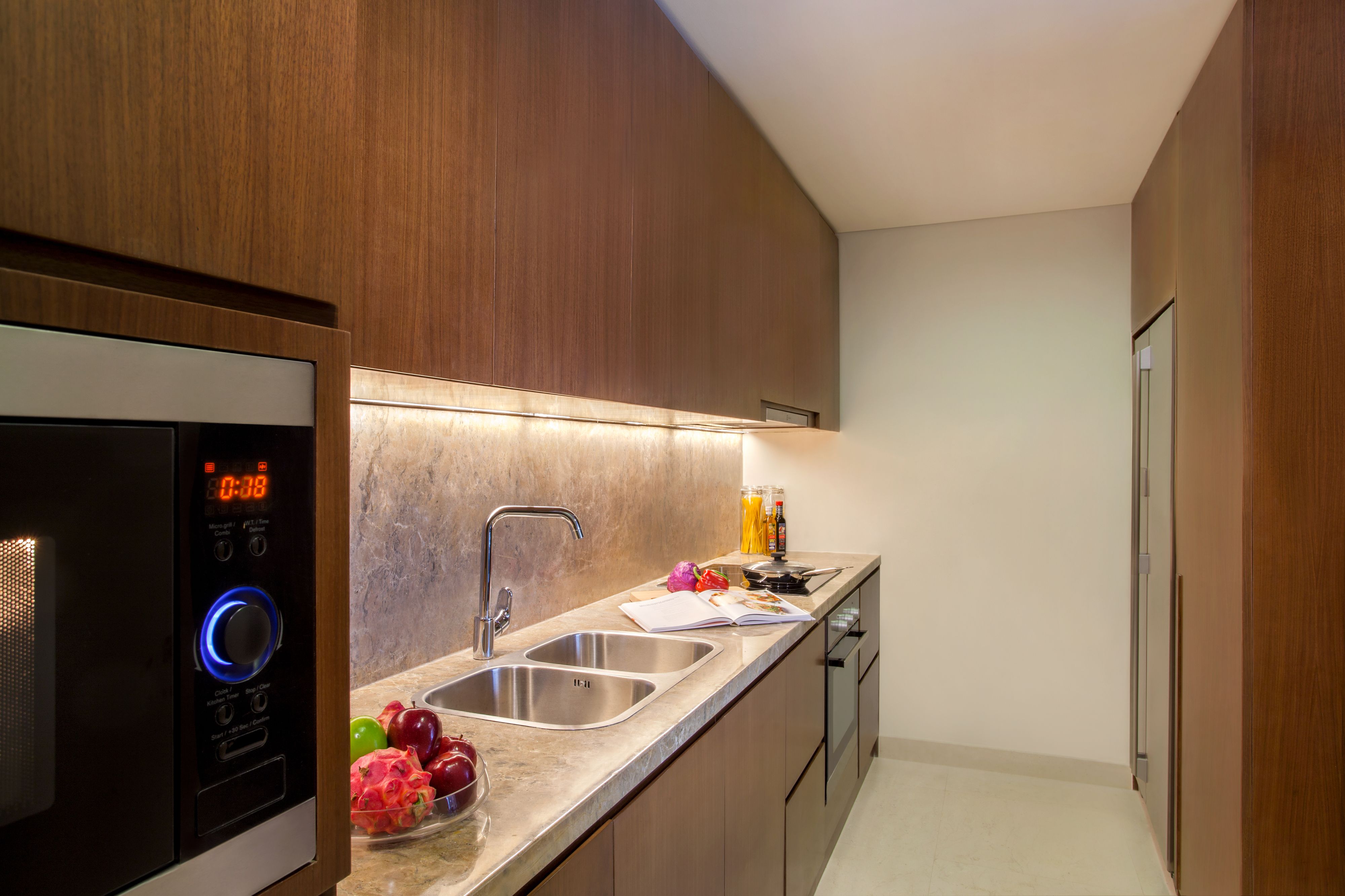 A modern kitchen with a built-in microwave, stainless steel sink, and wooden cabinets.
