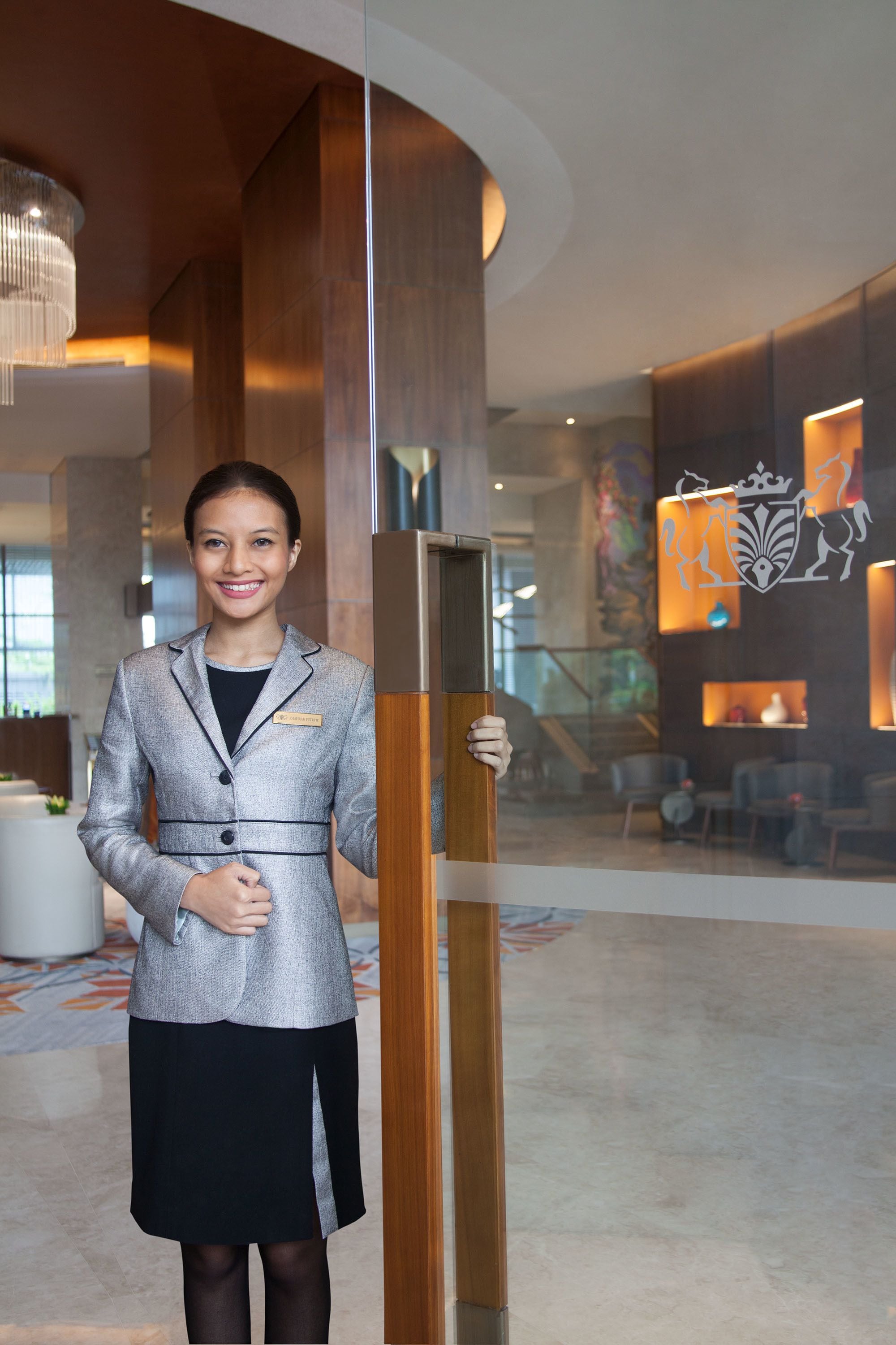 A person standing in a lobby with a modern interior design, including a large wooden column and a glass partition.