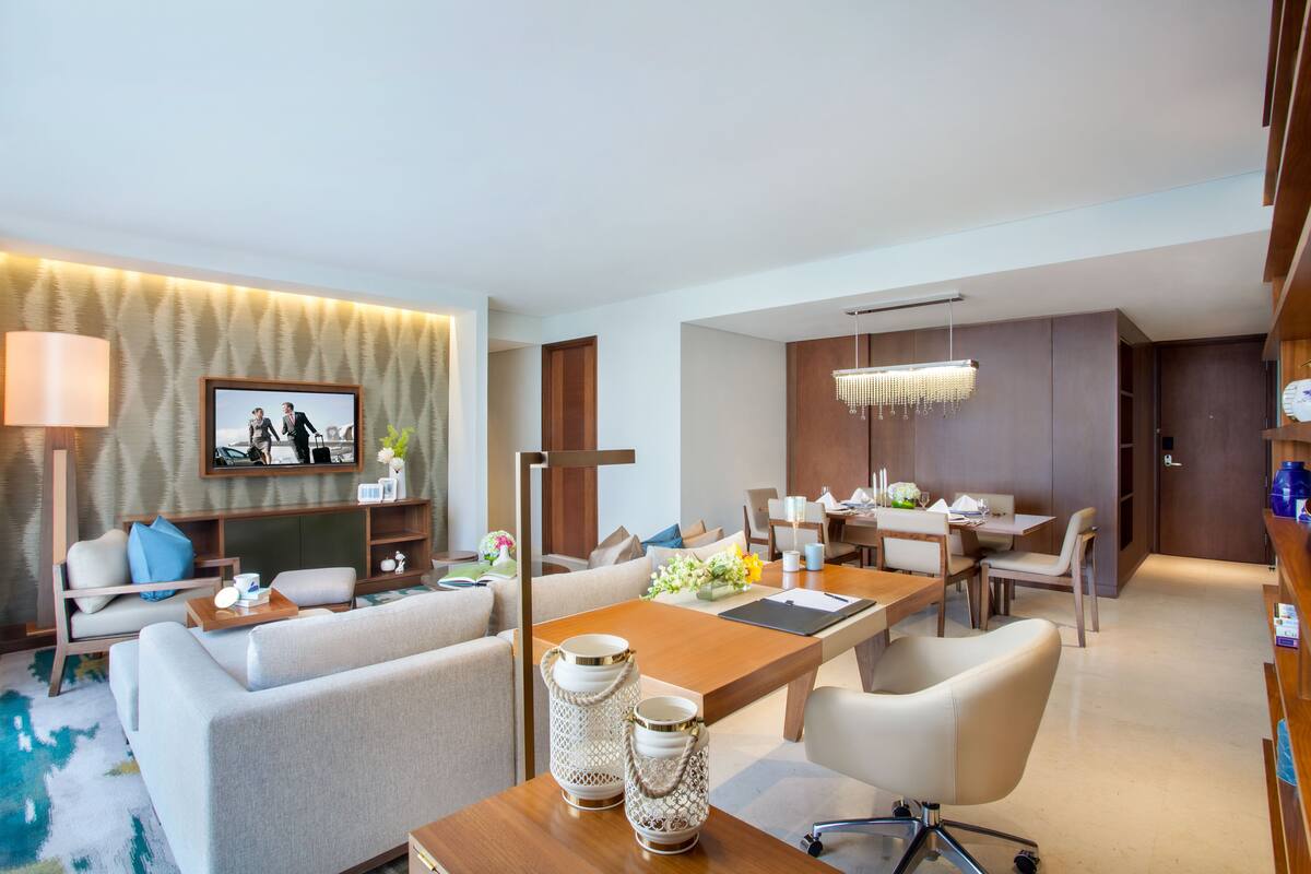 A modern hotel room with a living area, dining space, and a separate bedroom.