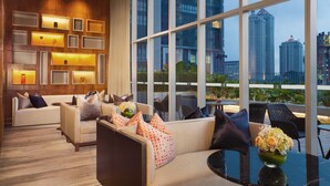 A modern hotel lobby with a sofa set, a table with a vase of flowers, and large windows offering a city view. - Ascott Sudirman Jakarta (Jakarta)