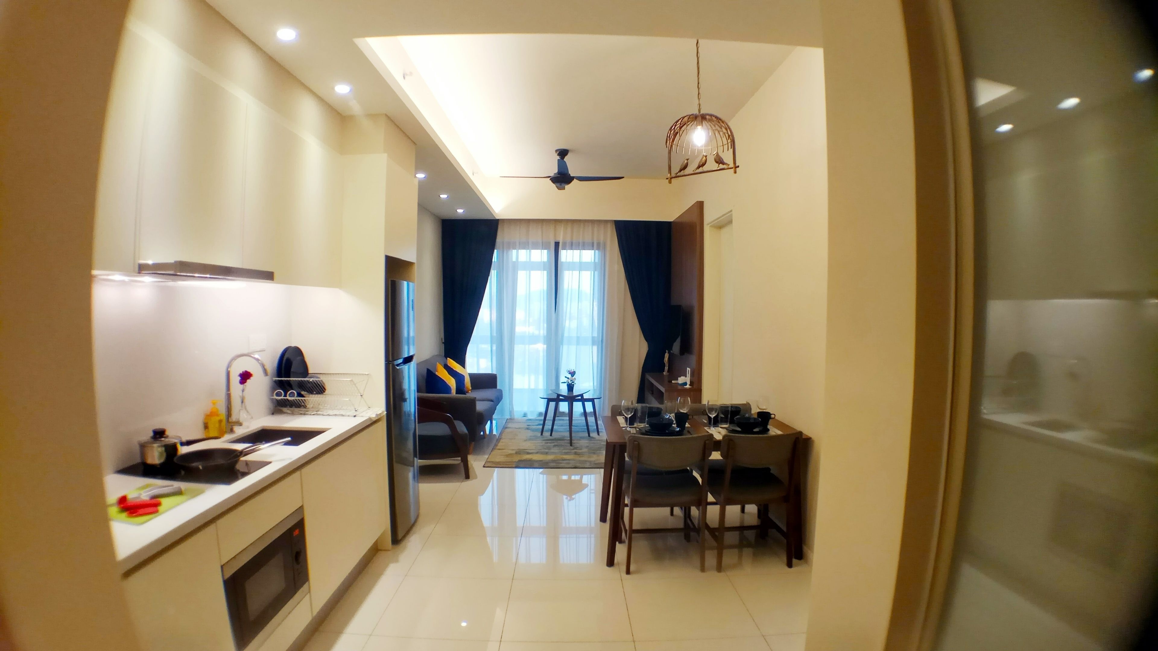 A modern kitchen with a refrigerator, microwave, and sink. There is a dining area with a table and chairs, and a ceiling fan above.